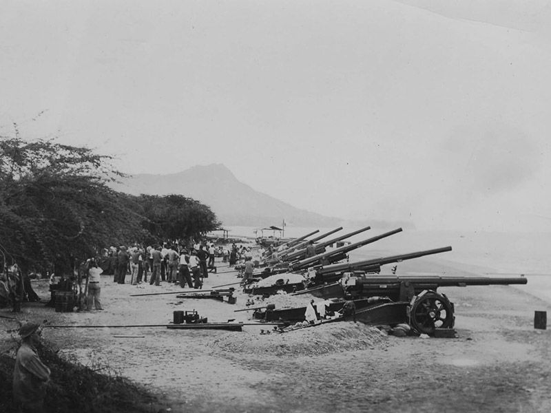 A black and white photo of a row of cannons on a beach