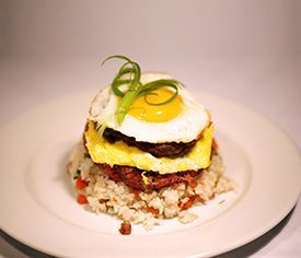 A white plate topped with a hamburger , eggs , and rice.