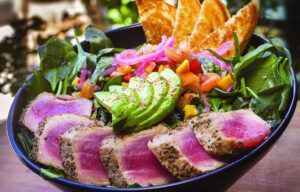 A close up of a bowl of food with meat and vegetables on a table.