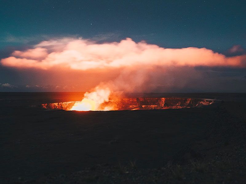 A volcano is erupting in the middle of a field at sunset.