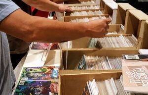A group of people are standing around a table looking at comic books.