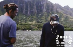 Two men are standing next to a body of water with mountains in the background.