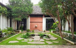A courtyard with a stone walkway leading to a building surrounded by trees and grass.