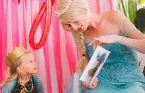 A woman dressed as elsa is reading a book to a little girl.