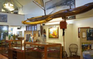A museum with a display case and a large wooden object hanging from the ceiling.