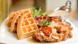 A plate of food with waffles and chicken on a table.