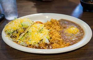 A plate of mexican food with tacos , rice and beans on a table.