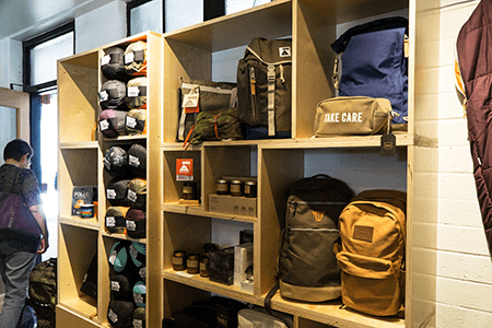 A man is standing in front of a shelf filled with backpacks and hats.
