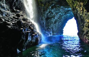 A waterfall is coming out of a cave into the ocean.