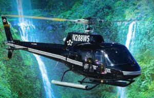 A black helicopter with n2888ws on the side is flying over a waterfall.