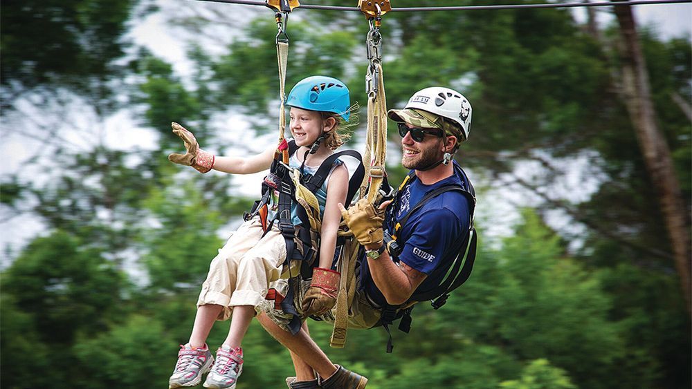 A man and a little girl are riding a zip line.