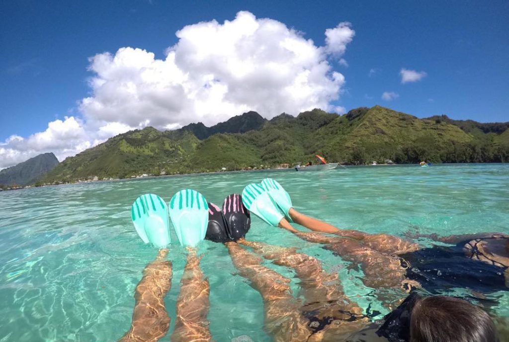A couple of people are swimming in the ocean with their feet in the water.