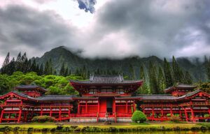 There is a temple in the middle of a forest with mountains in the background.