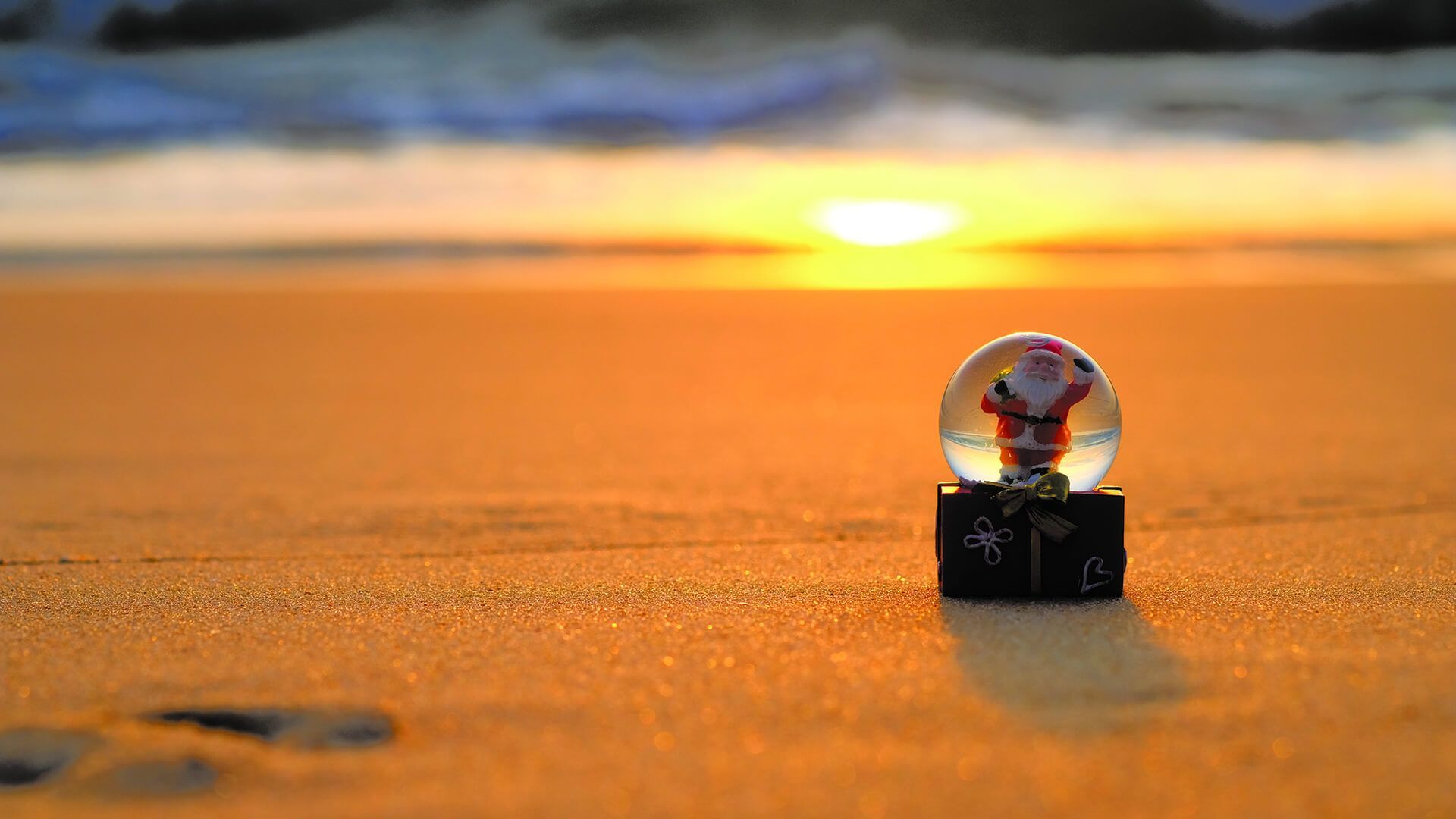 A snow globe with santa claus on it is on the beach at sunset.