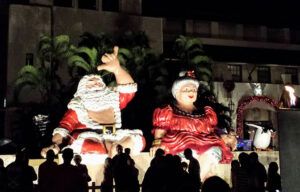 A group of people are standing in front of a statue of santa claus and mrs claus.