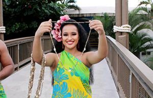 A woman in a hawaiian dress is holding a necklace on a bridge.