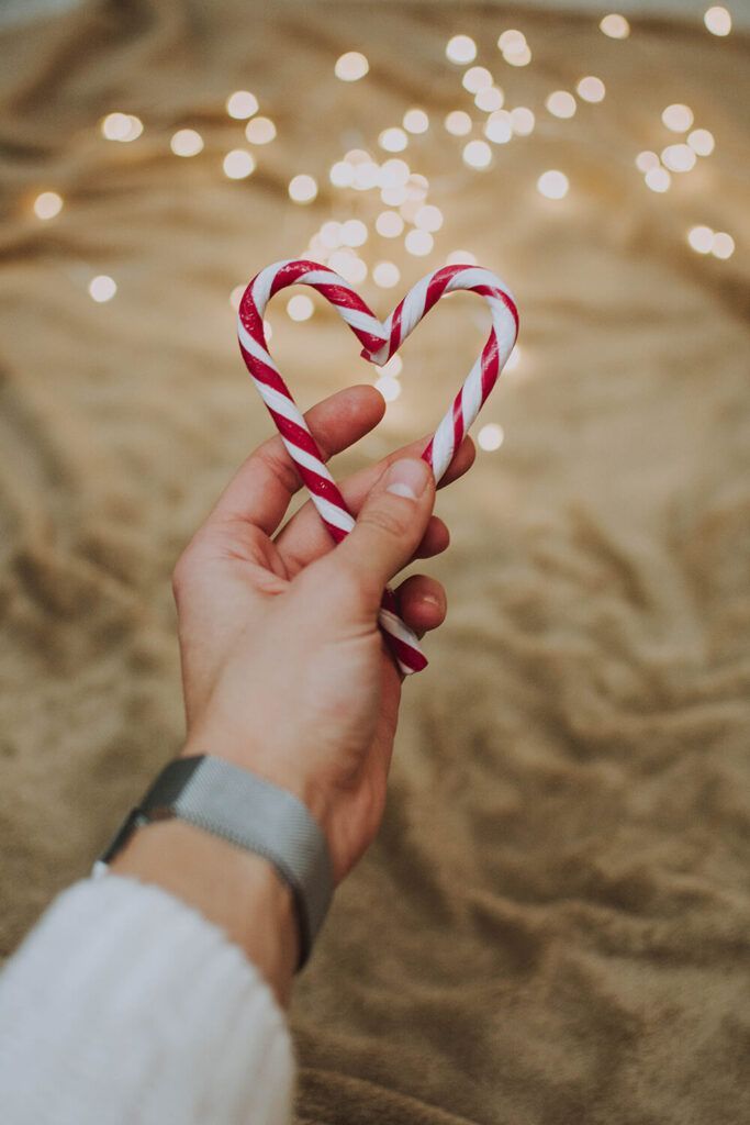 A person is holding a heart shaped candy cane in their hand.