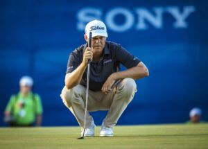 A man is squatting down on a golf course holding a golf club.