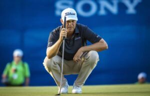 A man is kneeling down on a golf course holding a golf club.