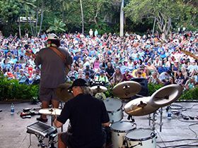 A man is playing drums on a stage in front of a large crowd.