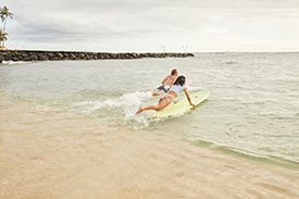 A man and a woman are riding a wave on a surfboard on the beach.