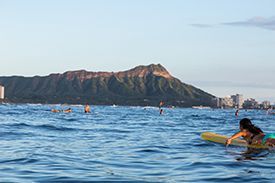 A woman is riding a surfboard in the ocean with a mountain in the background.