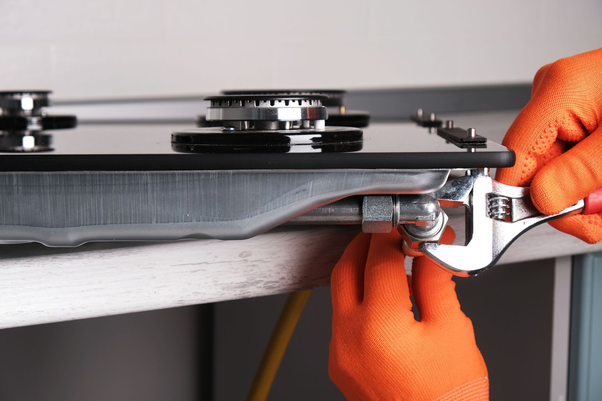 Gloved hands using a wrench to adjust a metal mechanism under a tabletop machine