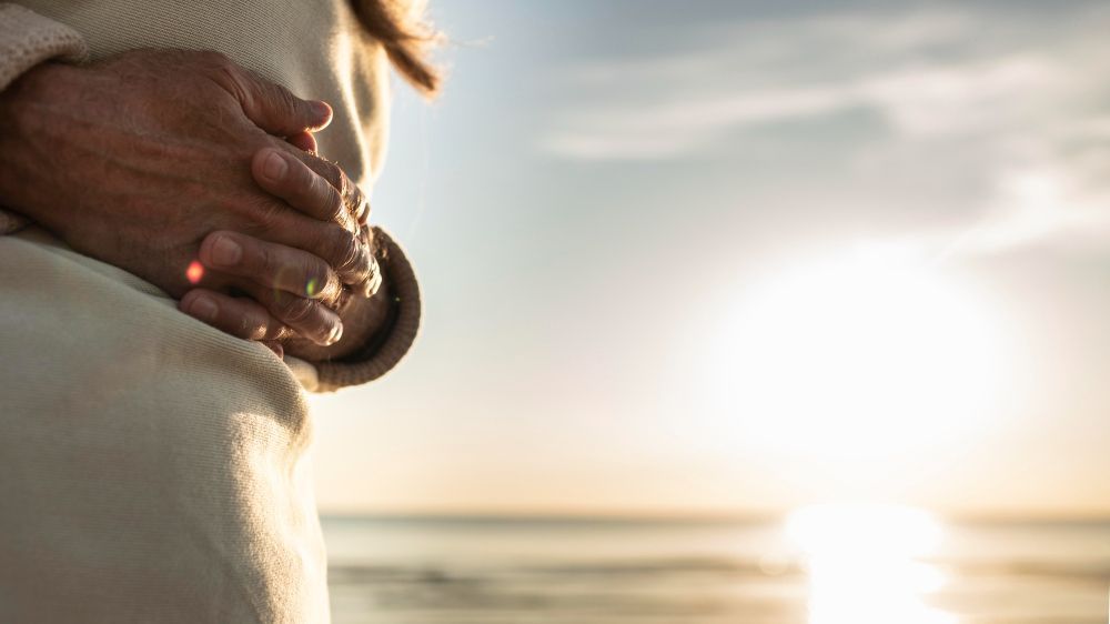 A person is standing on the beach with their hands folded in prayer.