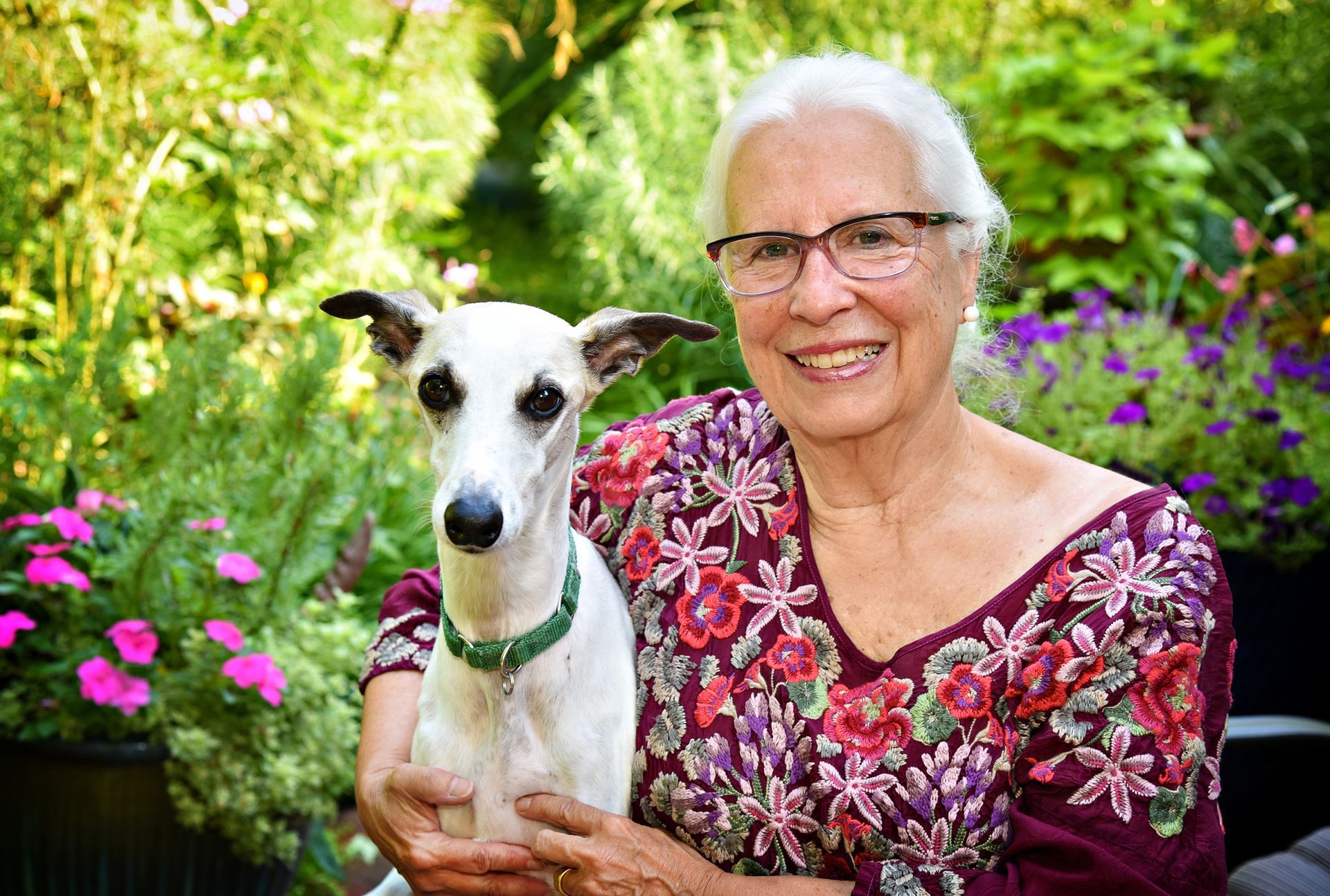 An elderly woman is holding a small white dog in her arms.