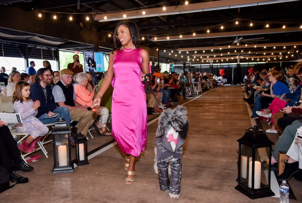 A woman is walking a dog down a runway at a fashion show.