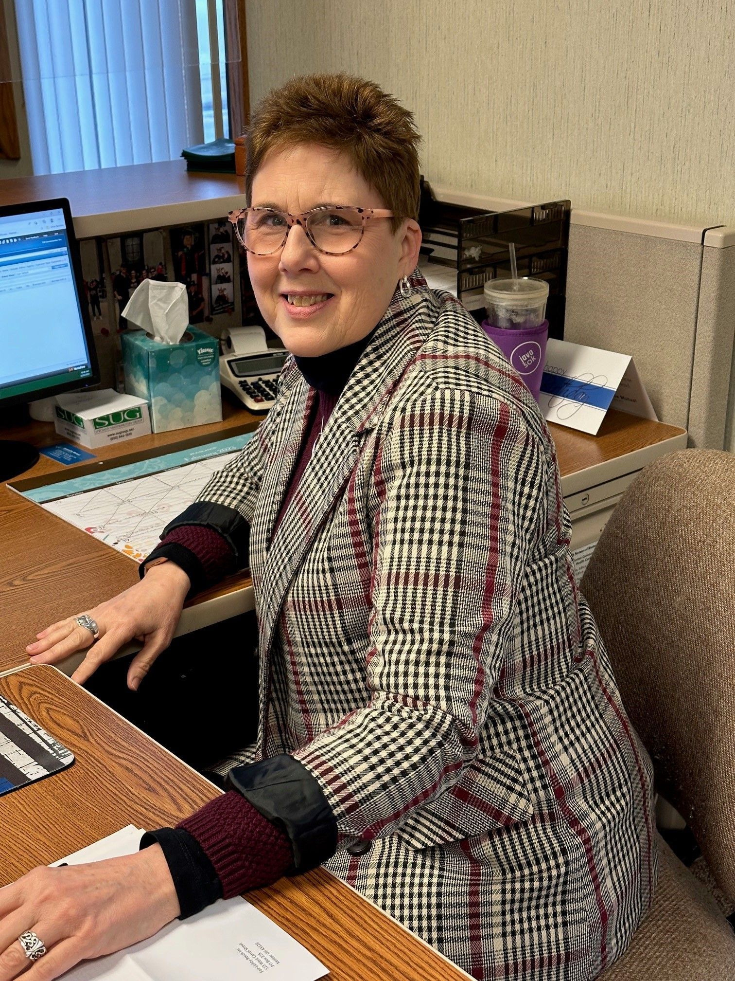 A woman wearing glasses is sitting at a desk in front of a computer.