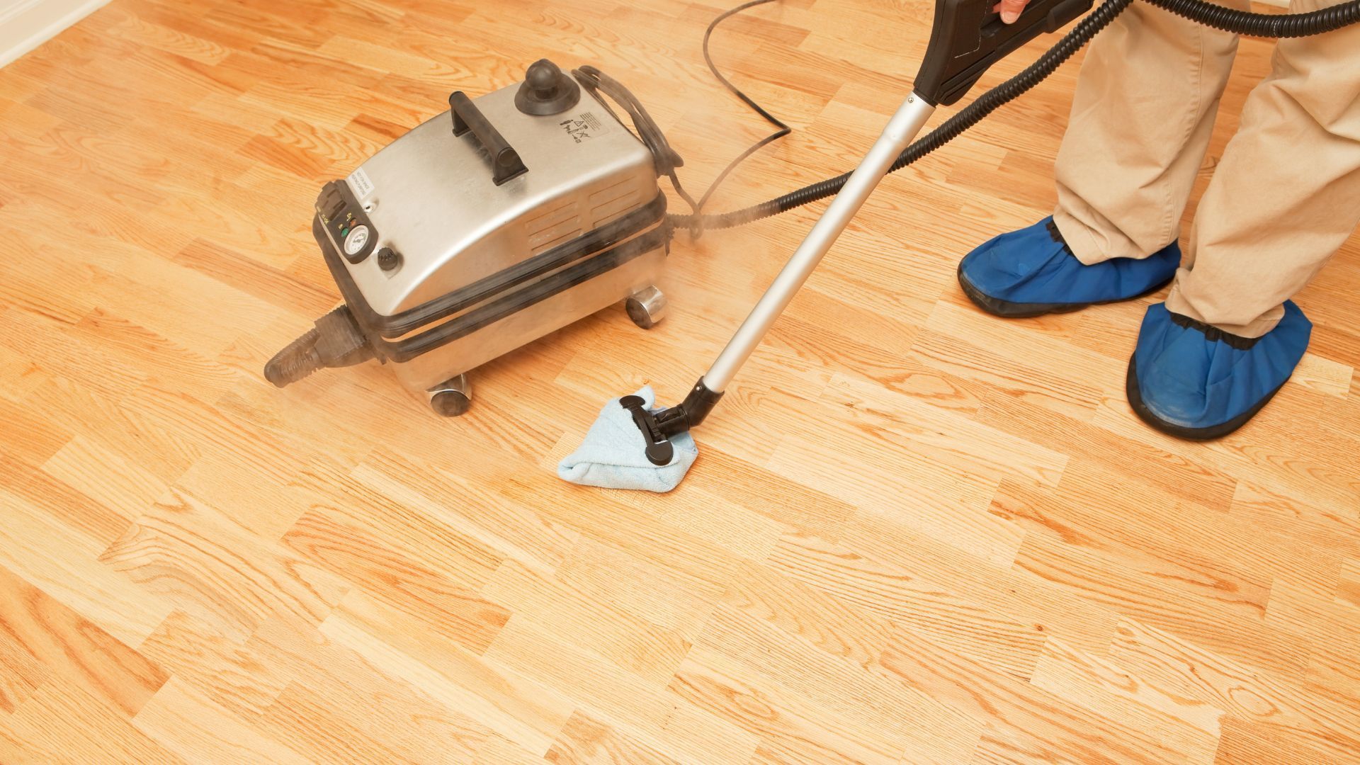 A person is using a steam mop to clean a wooden floor.