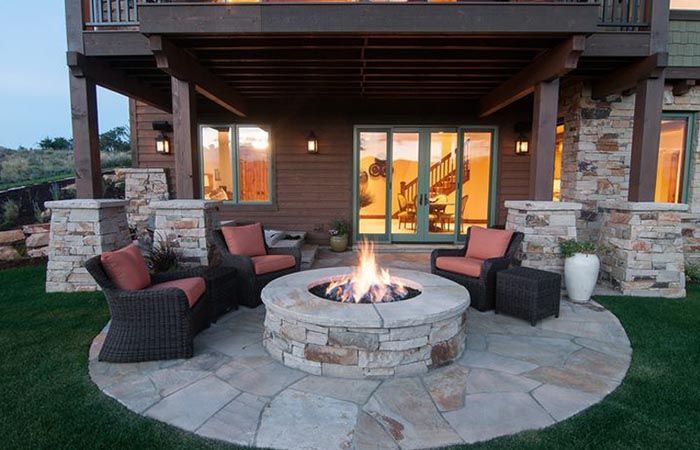 Stone fire pit with four chairs on a patio, under a wooden deck.