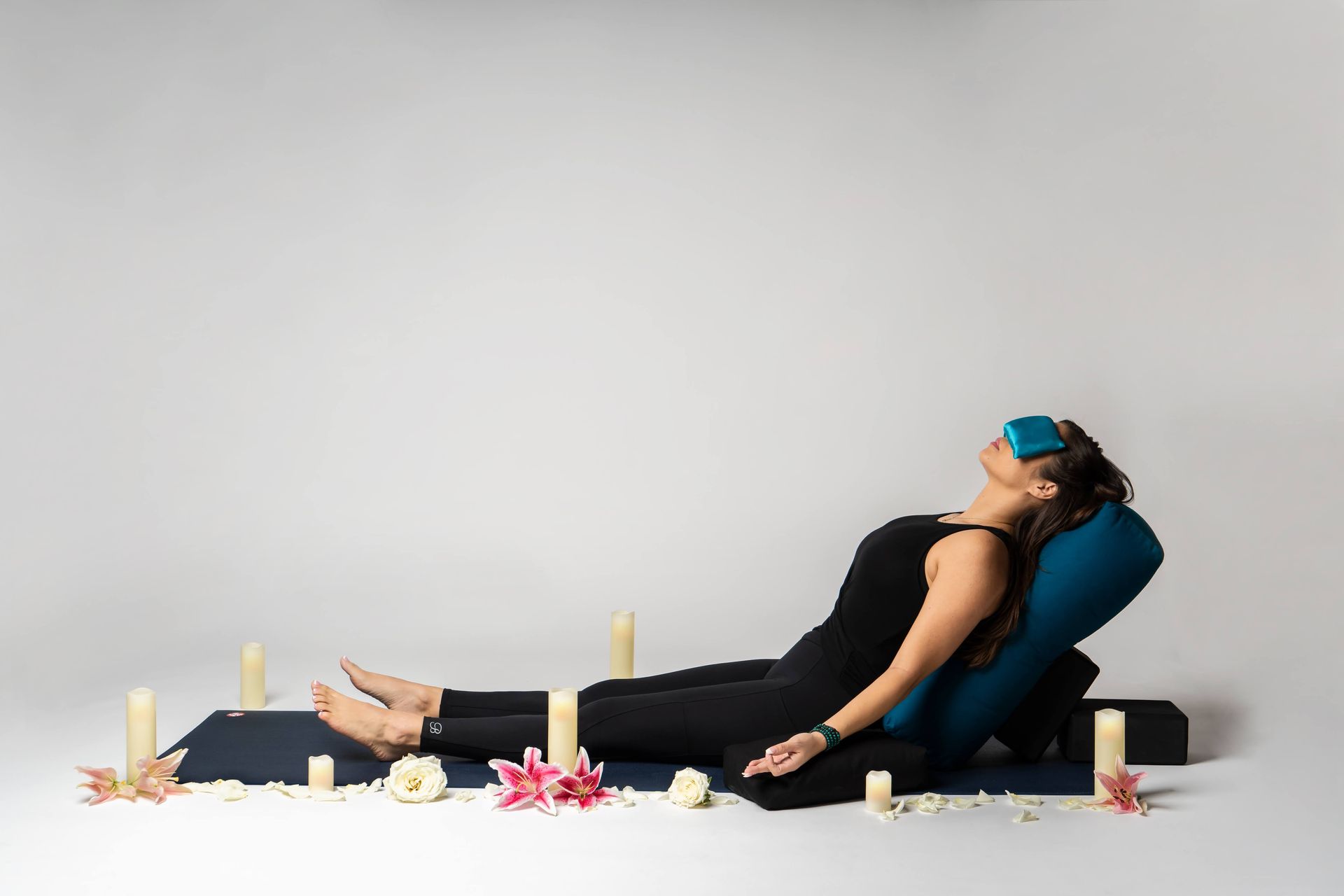A woman is laying on a yoga mat with candles around her.