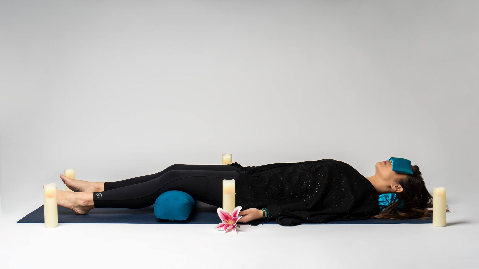 A woman is laying on a yoga mat with candles around her.