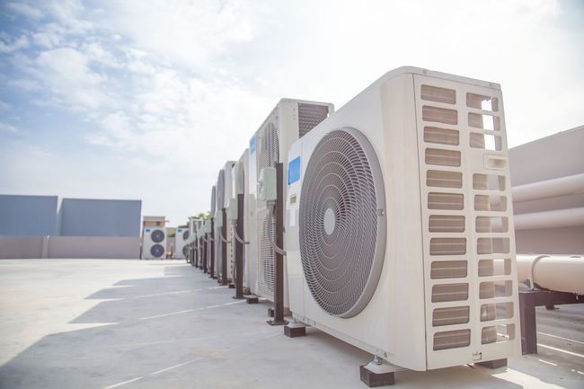 Row of large rooftop HVAC units on a sunlit industrial roof under a bright sky