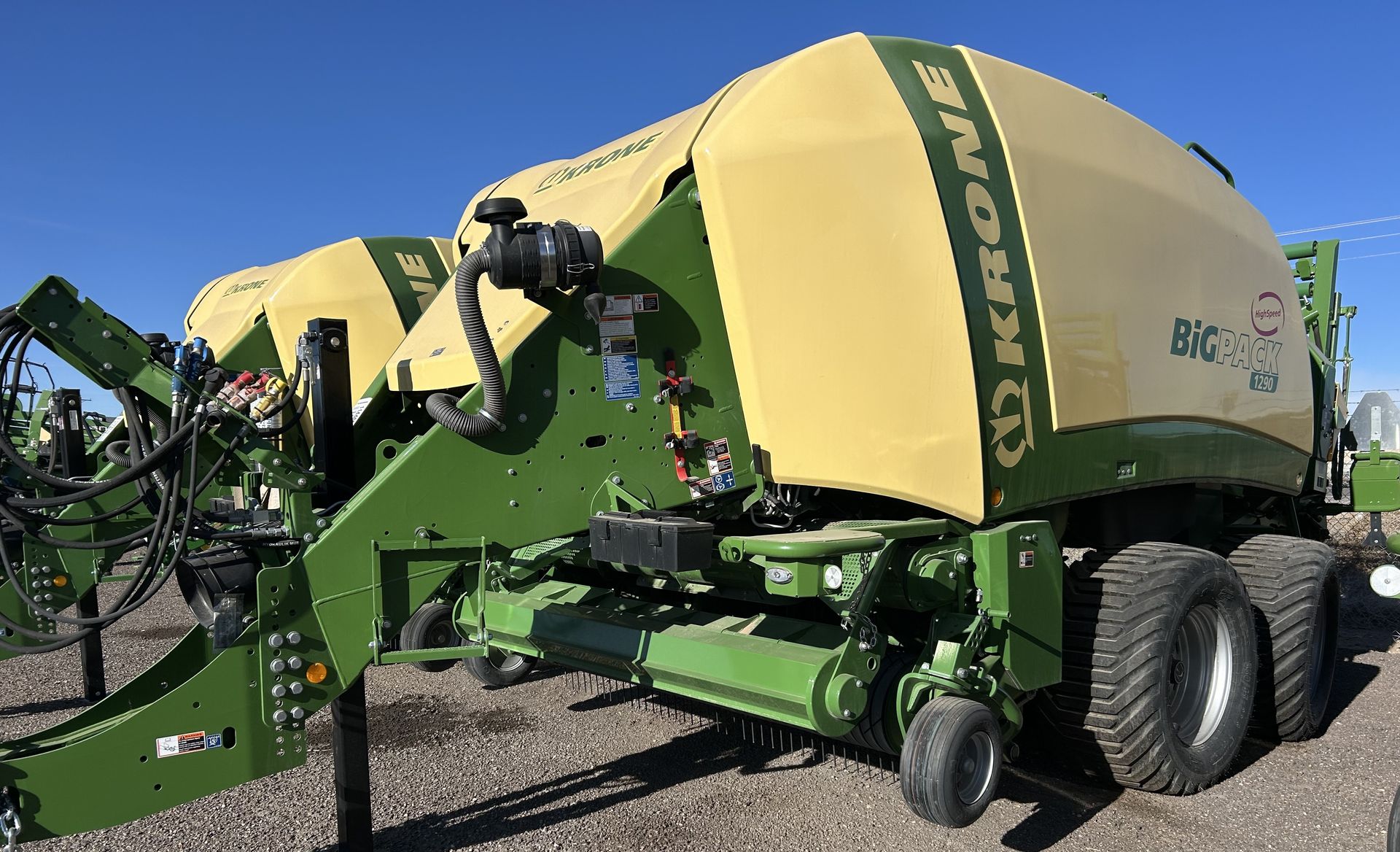 A yellow and green Krone BiG Pack square baler parked outdoors on a gravel lot under a clear blue sky.