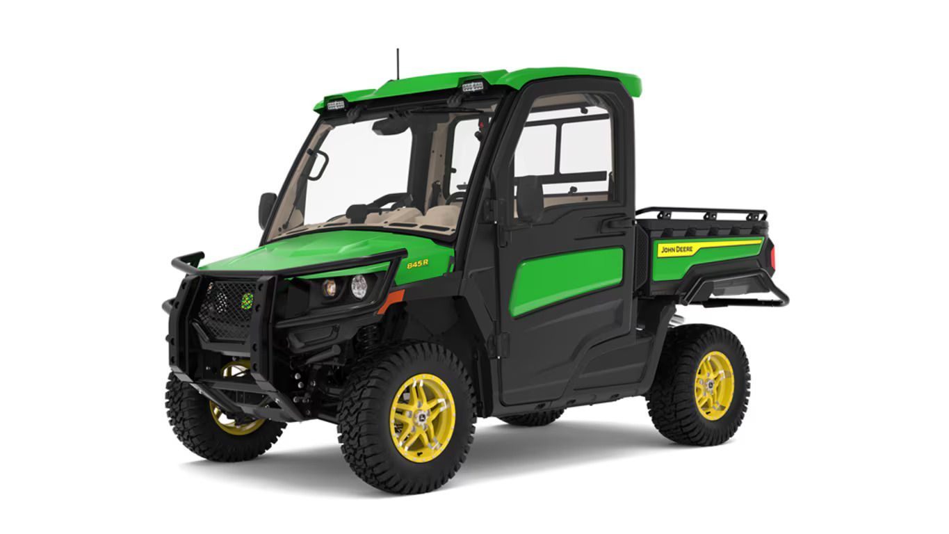 A green and black John Deere Gator utility vehicle with a full cab and cargo bed against a white background.