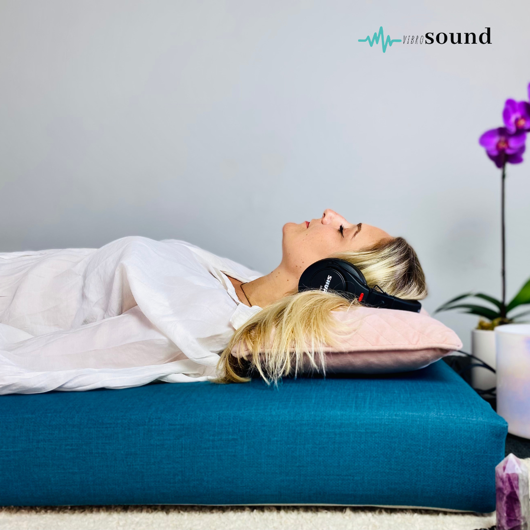 Woman reclining on a couch, hugging a pink pillow and wearing headphones, smiling.