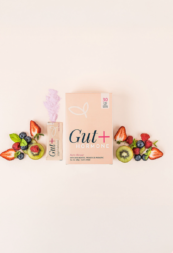A box of Gut+ Hormone supplement powder with a single sachet, surrounded by fresh strawberries, kiwi, and blueberries.