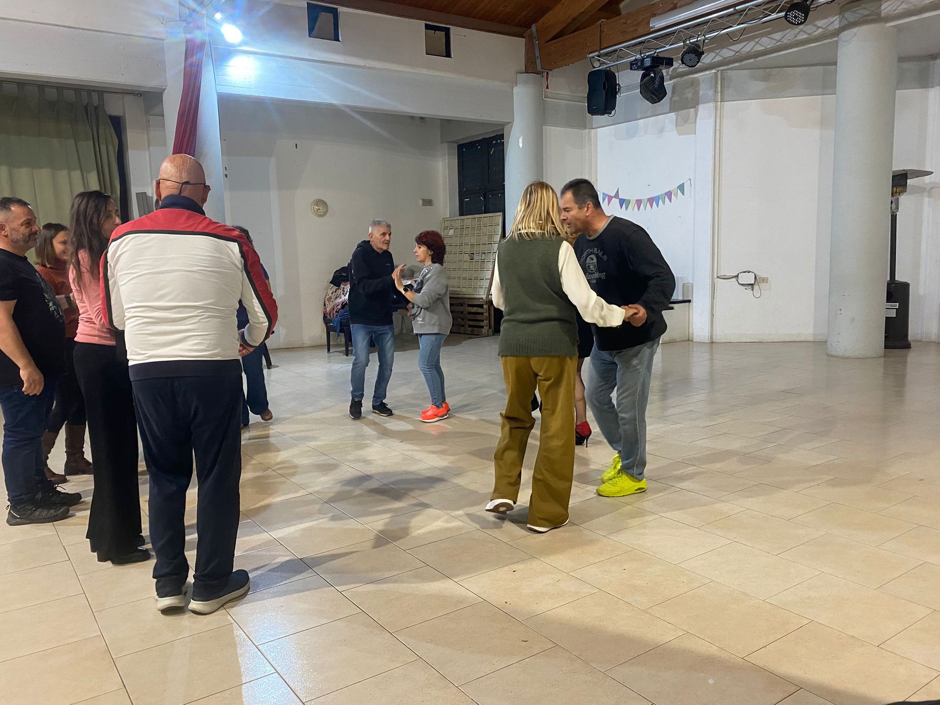 Persone che ballano in una stanza ben illuminata con pavimento in legno.