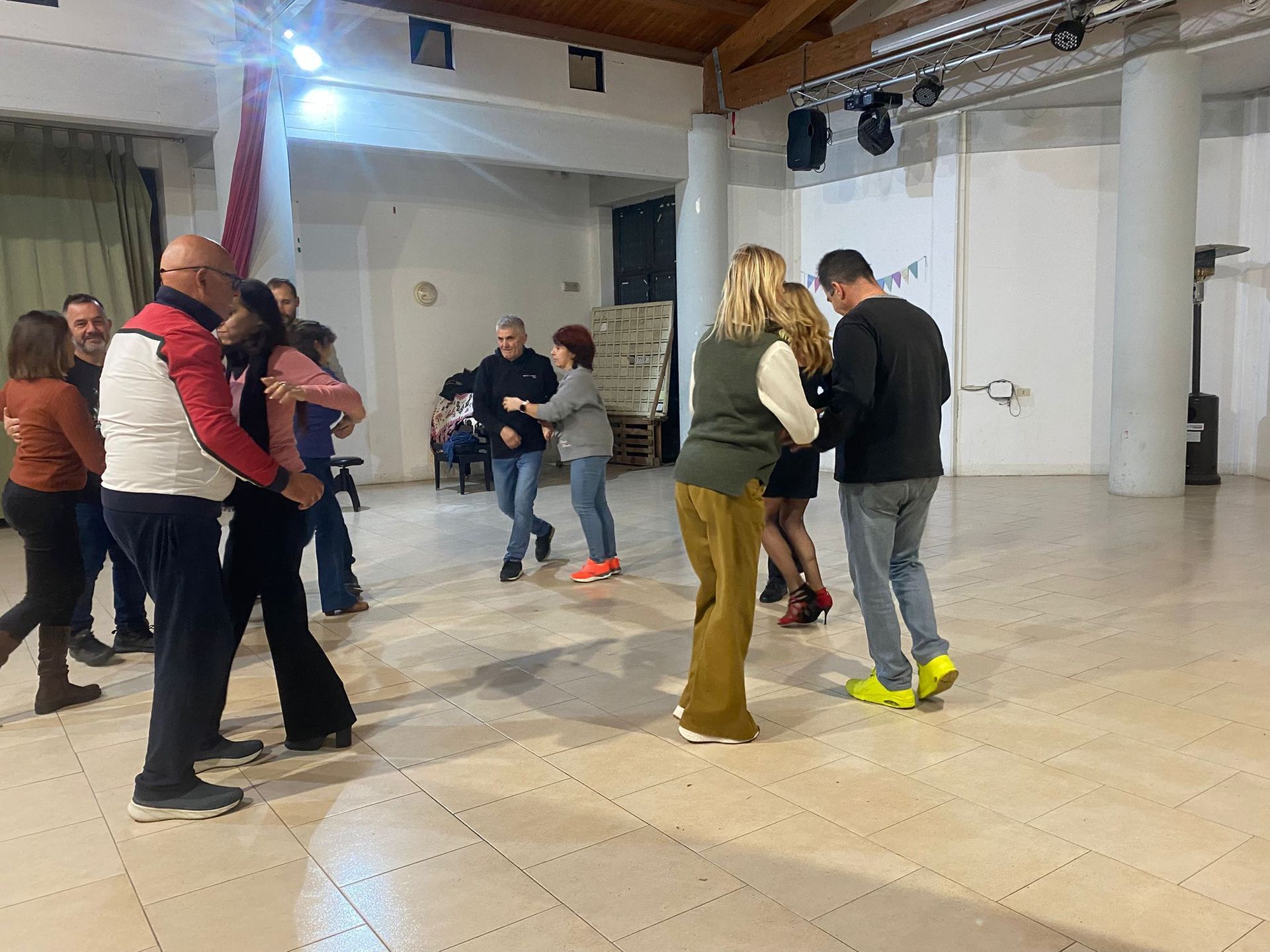 Persone che ballano in una stanza illuminata da una palla da discoteca. Diverse coppie in abiti casual.