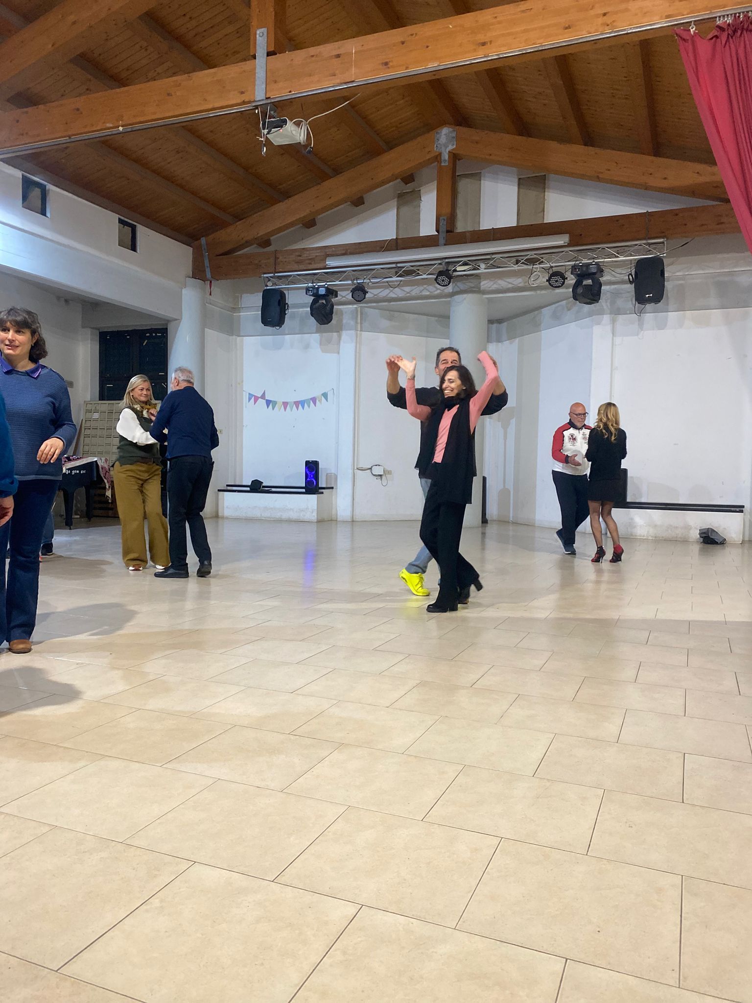 Persone che ballano in una spaziosa sala con travi in legno. Una persona alza le braccia in segno di eccitazione.