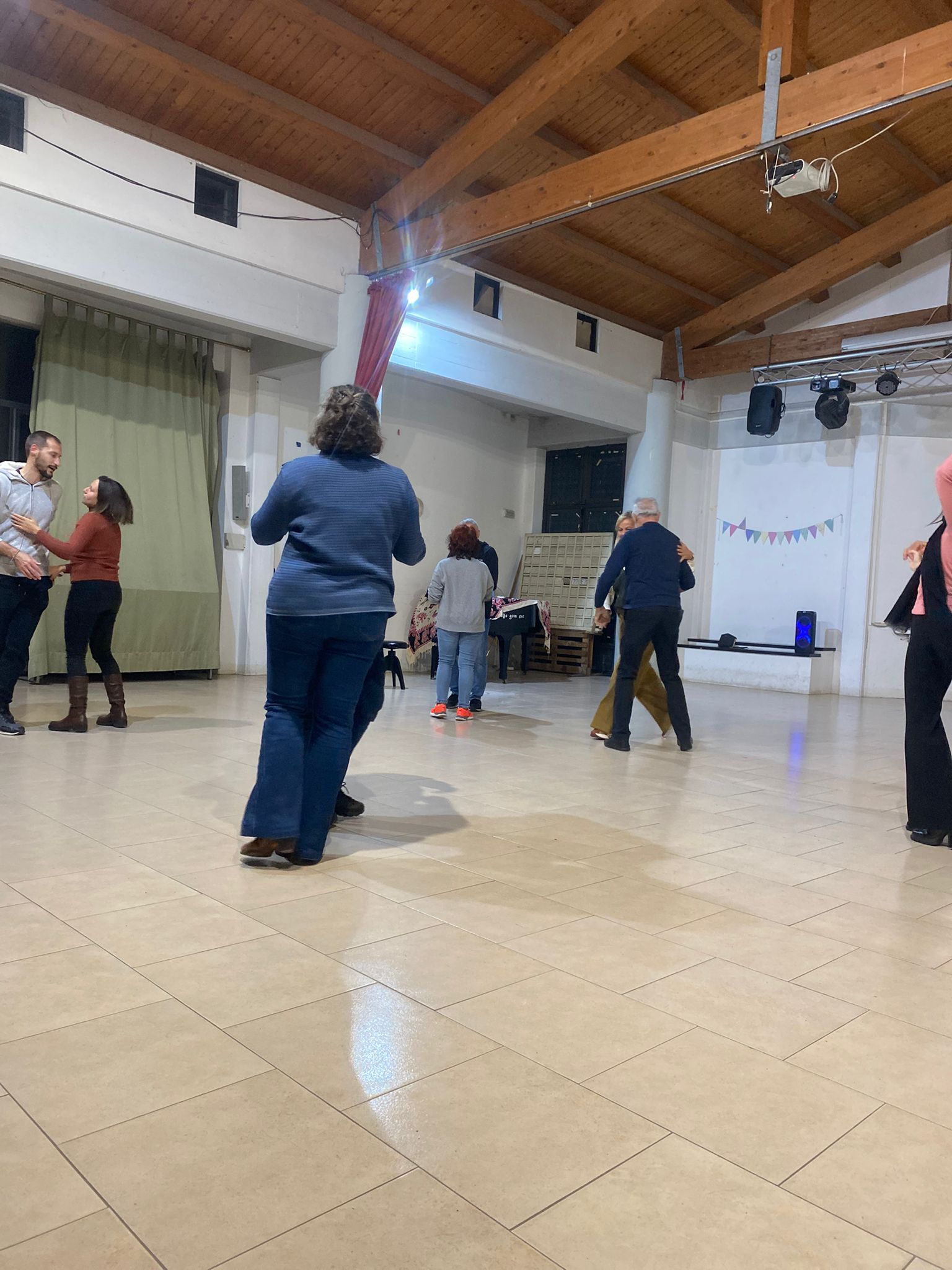 Persone che ballano in una spaziosa sala con travi in legno e pavimento piastrellato.