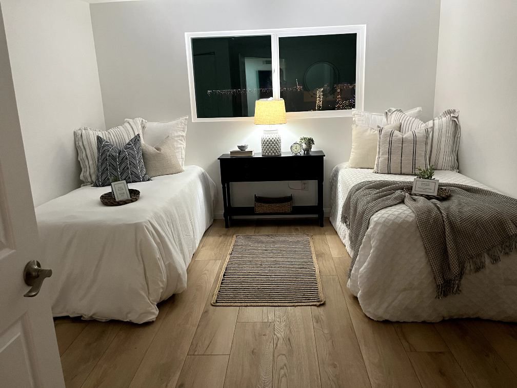 Two twin beds in a room with a window, nightstand, and rug. White bedding, neutral decor.