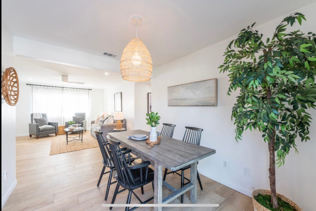 Dining room with wooden table, black chairs, pendant light, and faux tree.