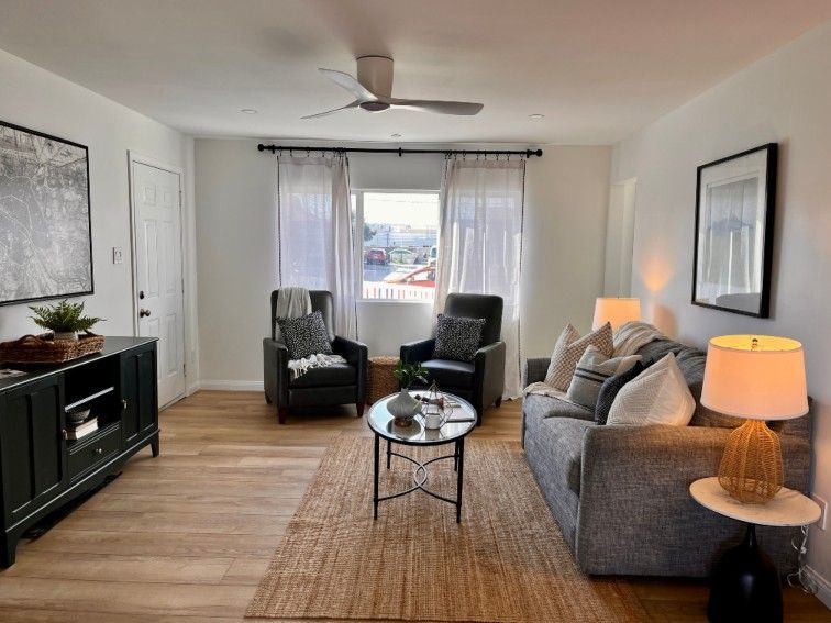Living room with gray sofa, black armchairs, and a neutral rug; white walls, window with sheer curtains.