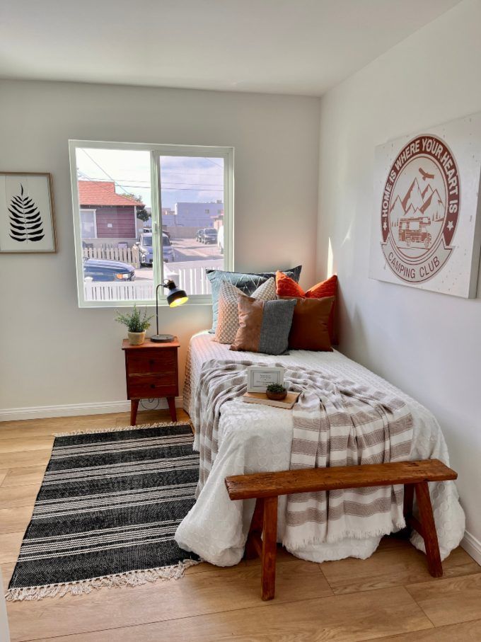 Bedroom with a single bed, wooden nightstand, and bench, with a gray and brown striped rug.