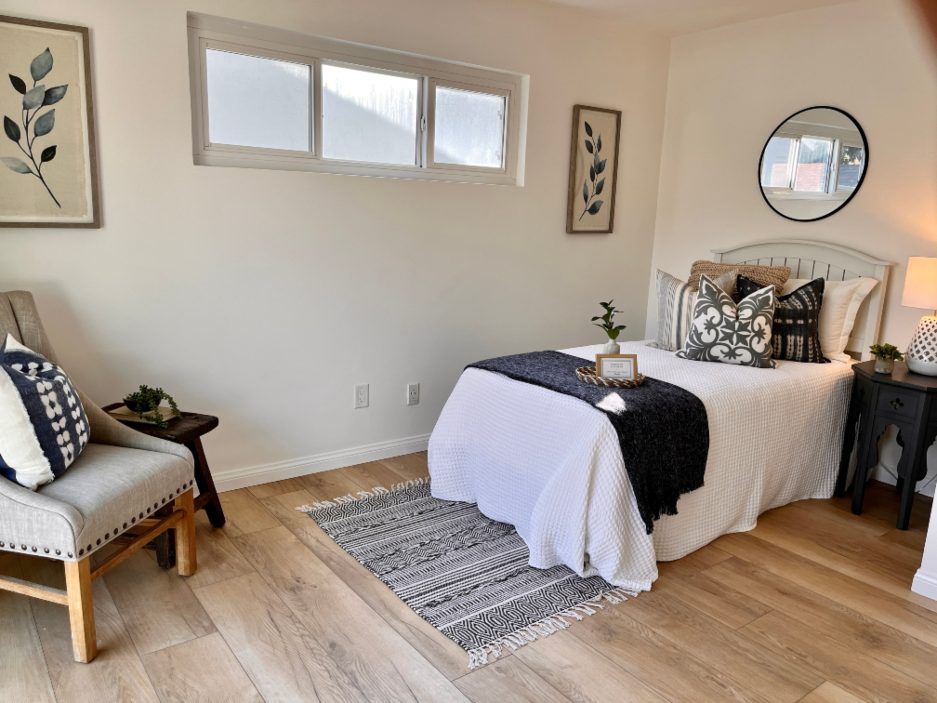 Bedroom with bed, chair, rug, plants, artwork, and wood floors.
