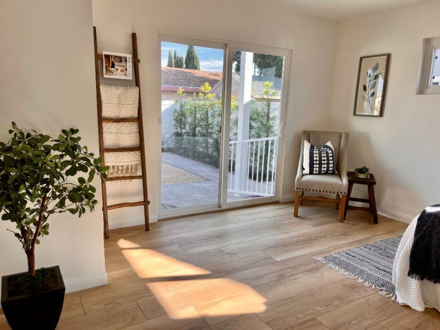 Bedroom with sliding glass door, wooden floors, and a ladder leaning against the wall.